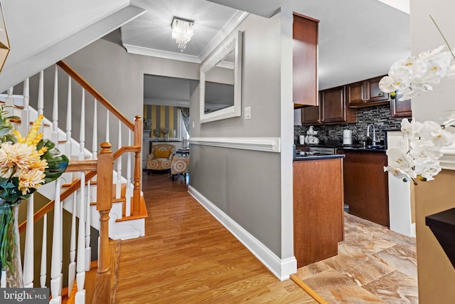 kitchen featuring a notable chandelier, light wood-type flooring, crown molding, backsplash, and sink