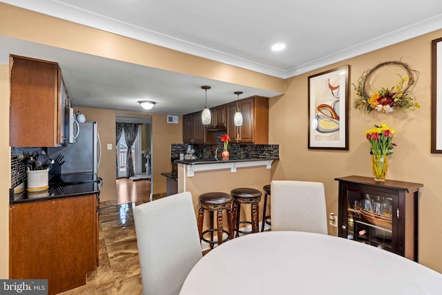 kitchen with kitchen peninsula, hanging light fixtures, ornamental molding, tasteful backsplash, and a kitchen breakfast bar