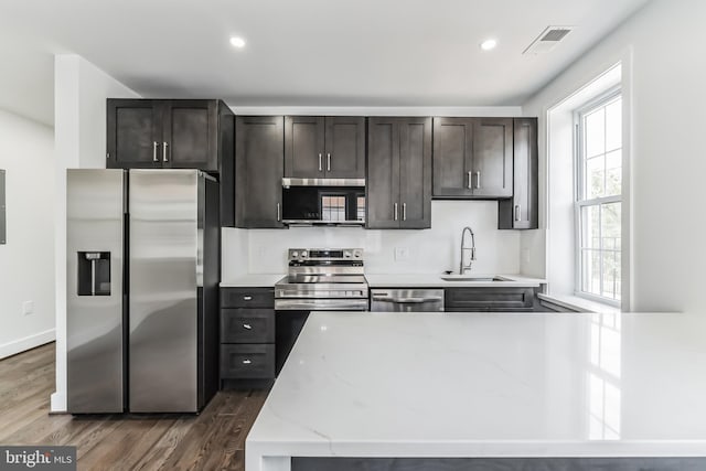 kitchen with stainless steel appliances, dark brown cabinetry, light stone countertops, sink, and dark wood-type flooring