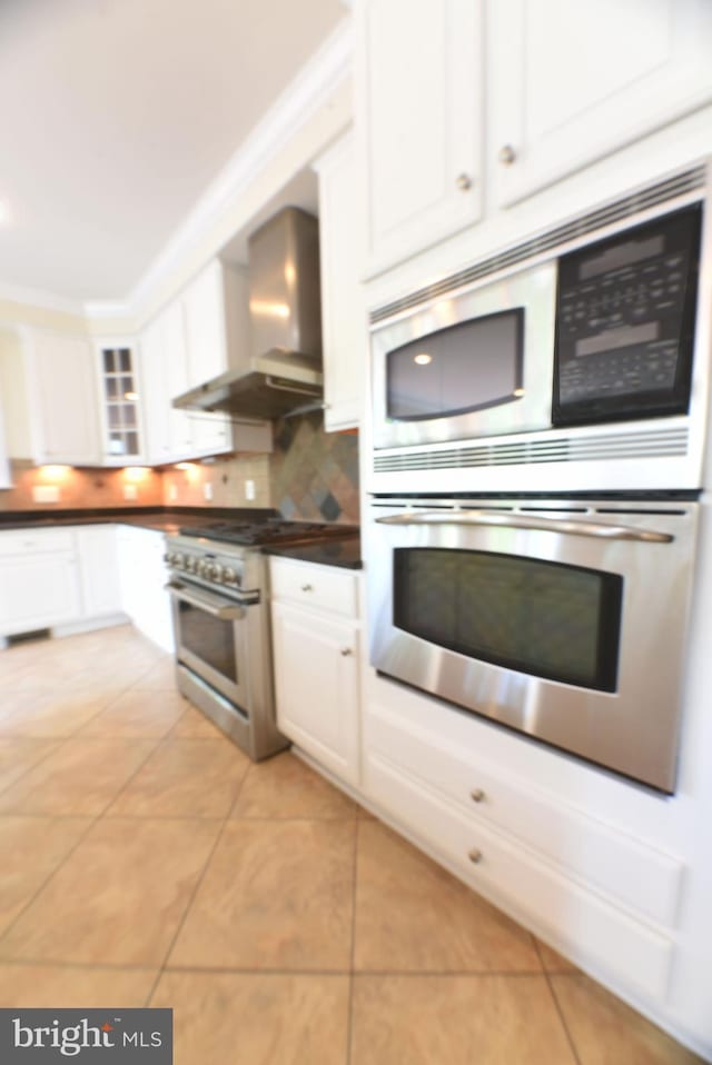 kitchen with appliances with stainless steel finishes, white cabinets, wall chimney exhaust hood, and light tile patterned floors