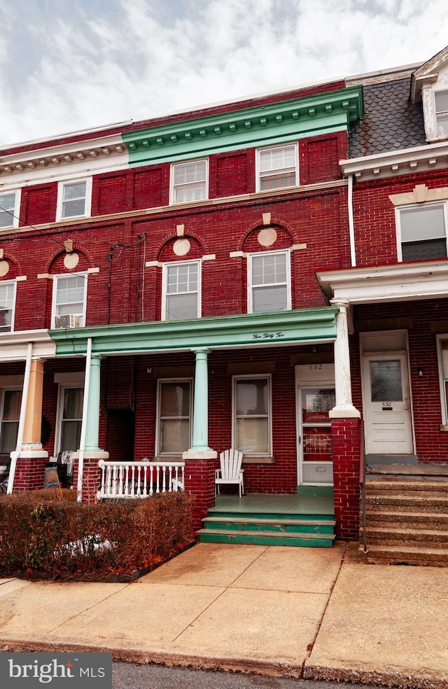 townhome / multi-family property with covered porch, mansard roof, and brick siding