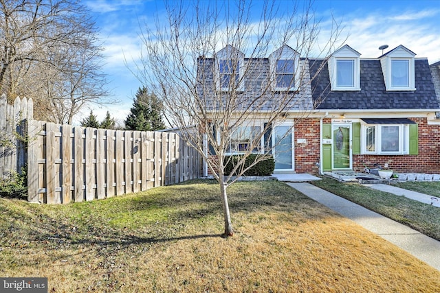 view of front of property featuring a shingled roof, a front yard, brick siding, and fence