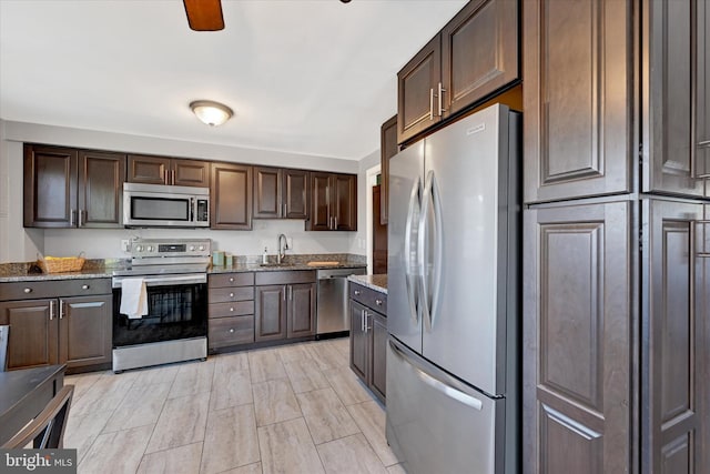 kitchen featuring stainless steel appliances, dark brown cabinets, a sink, and light stone countertops