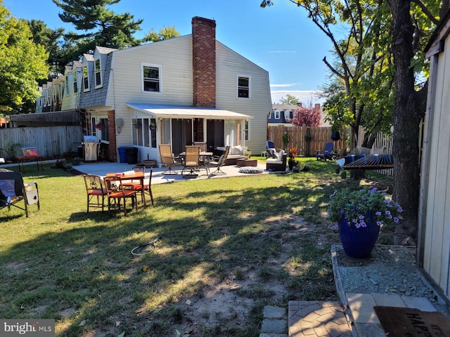 back of property featuring a chimney, fence, a lawn, and a patio