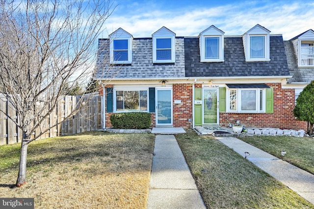 view of front of property featuring brick siding, a front yard, fence, and roof with shingles