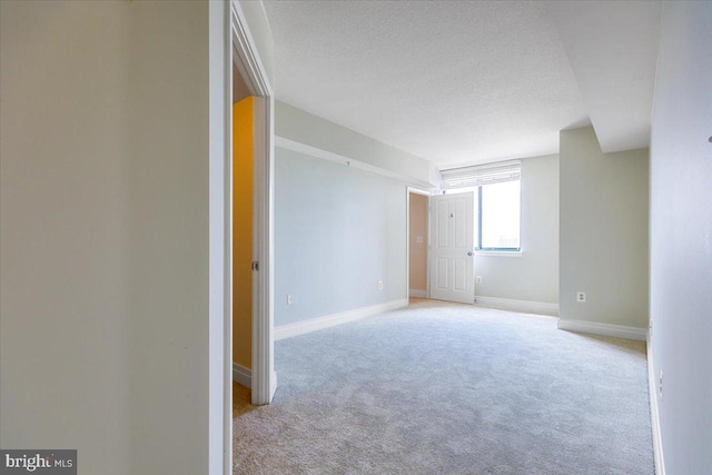 unfurnished room featuring baseboards, a textured ceiling, and light colored carpet