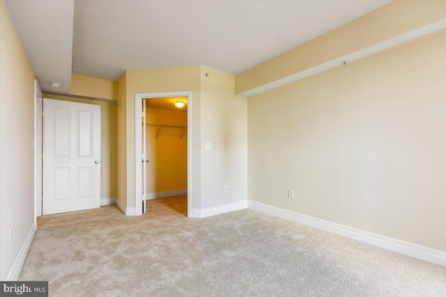 unfurnished bedroom with a walk in closet, a closet, light carpet, and baseboards