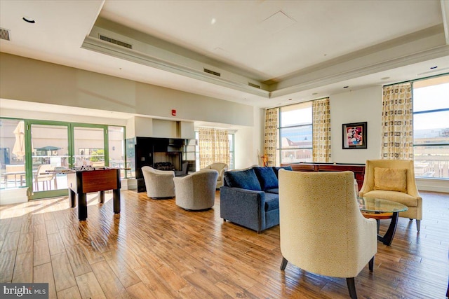 living room with a wealth of natural light, visible vents, a tray ceiling, and wood finished floors