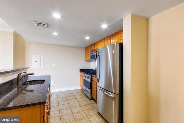 kitchen featuring stainless steel appliances, visible vents, brown cabinetry, a sink, and dark stone countertops