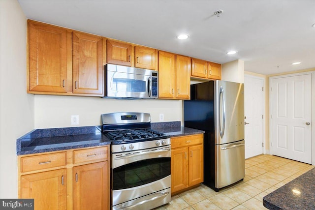 kitchen with light tile patterned floors, recessed lighting, stainless steel appliances, brown cabinetry, and dark stone countertops