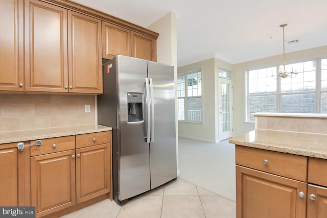 kitchen featuring light tile patterned floors, stainless steel refrigerator with ice dispenser, a notable chandelier, light stone counters, and pendant lighting