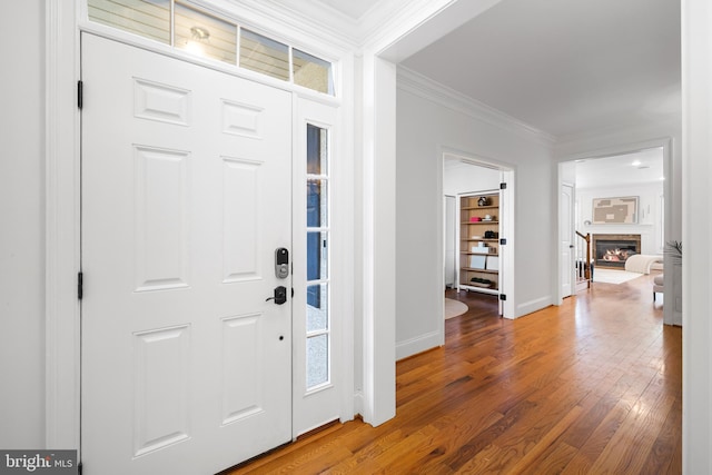 foyer with ornamental molding, a glass covered fireplace, wood-type flooring, and baseboards