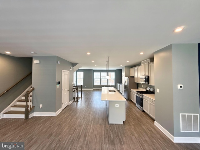 kitchen featuring dark wood-style floors, light countertops, a kitchen island with sink, visible vents, and stainless steel appliances