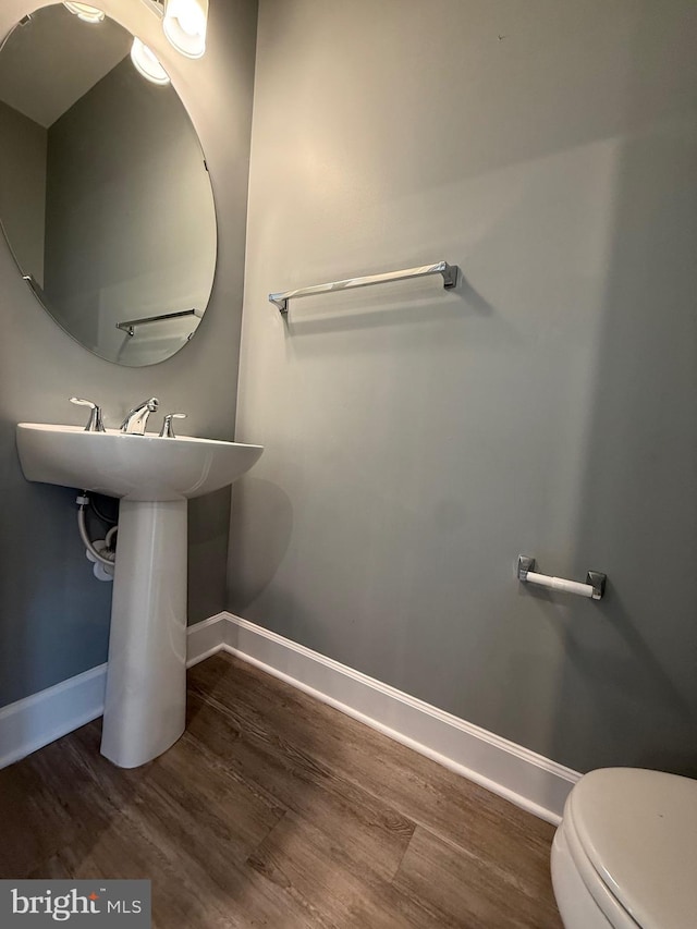 half bathroom with baseboards, toilet, and wood finished floors