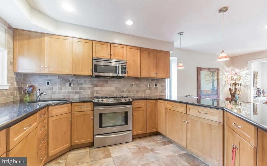 kitchen featuring kitchen peninsula, sink, backsplash, appliances with stainless steel finishes, and pendant lighting