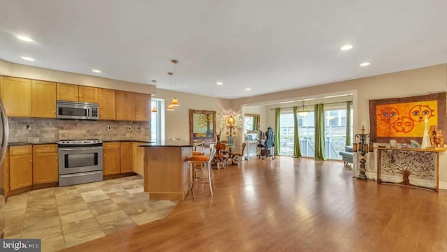 kitchen with appliances with stainless steel finishes, a kitchen breakfast bar, decorative backsplash, pendant lighting, and a kitchen island