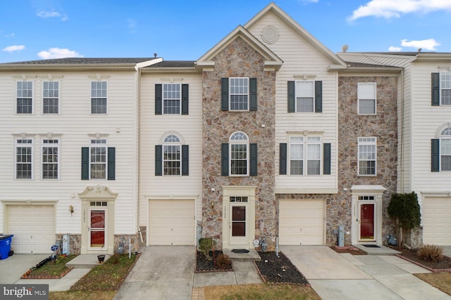 townhome / multi-family property with stone siding, driveway, and an attached garage