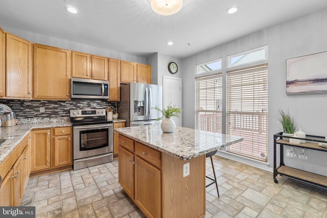 kitchen with stainless steel appliances, stone tile flooring, a kitchen island, and tasteful backsplash