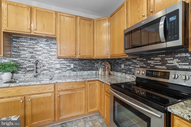 kitchen featuring decorative backsplash, light stone countertops, stone finish flooring, stainless steel appliances, and a sink