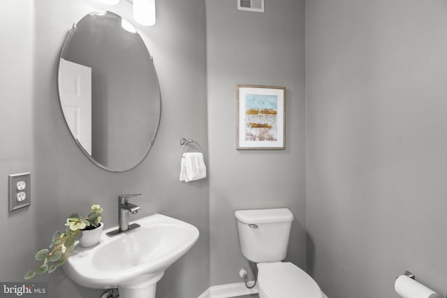 half bath with toilet, baseboards, visible vents, and a sink