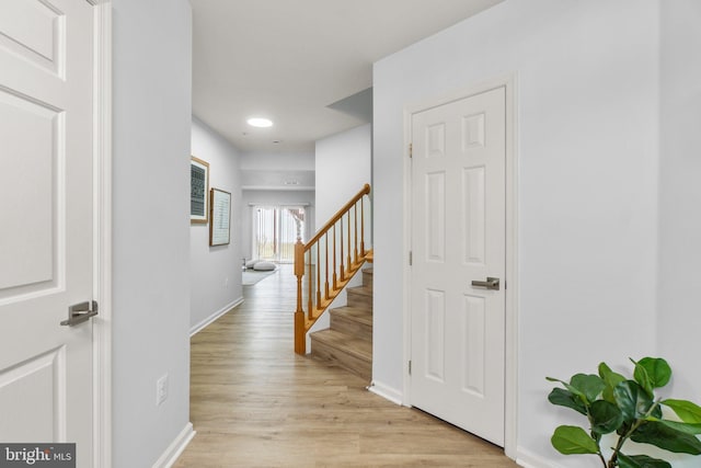 hallway with light wood-style flooring, stairway, and baseboards