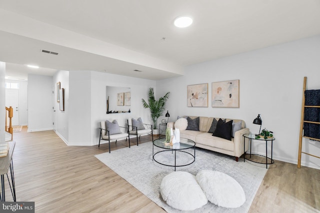 living area with light wood-type flooring, visible vents, stairway, and baseboards