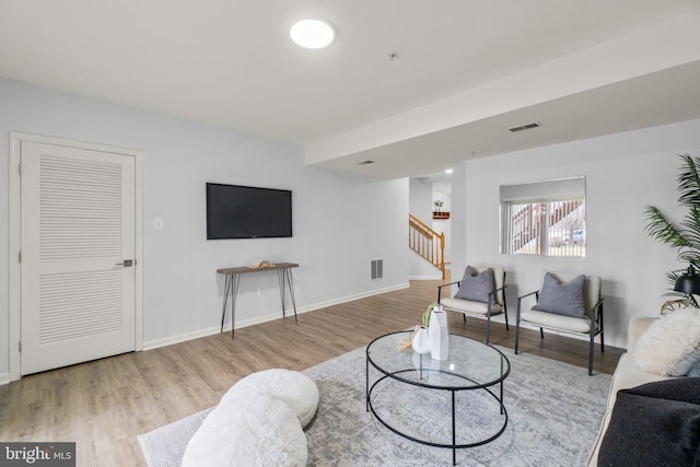 living area with stairs, baseboards, visible vents, and light wood-style floors