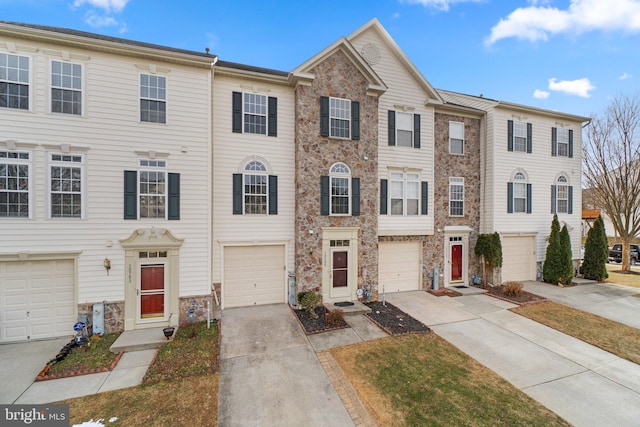 townhome / multi-family property with a garage, driveway, and stone siding