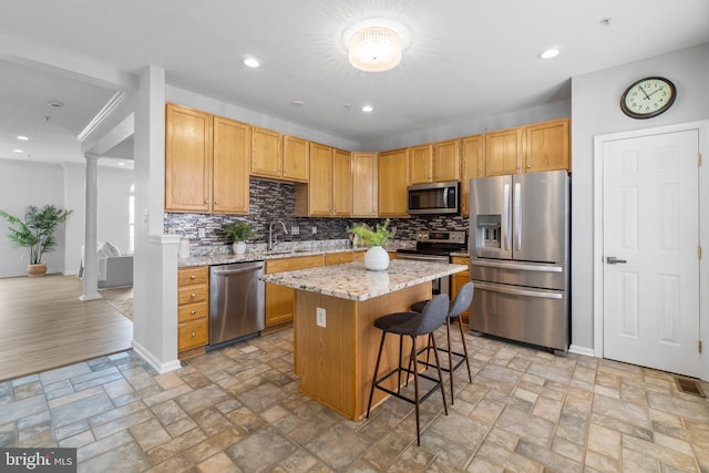 kitchen with decorative columns, stone finish floor, appliances with stainless steel finishes, a center island, and light stone countertops