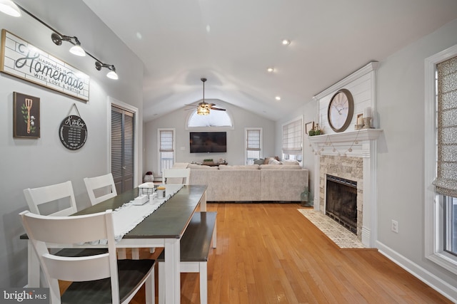 dining area featuring baseboards, a ceiling fan, a tile fireplace, vaulted ceiling, and light wood-type flooring