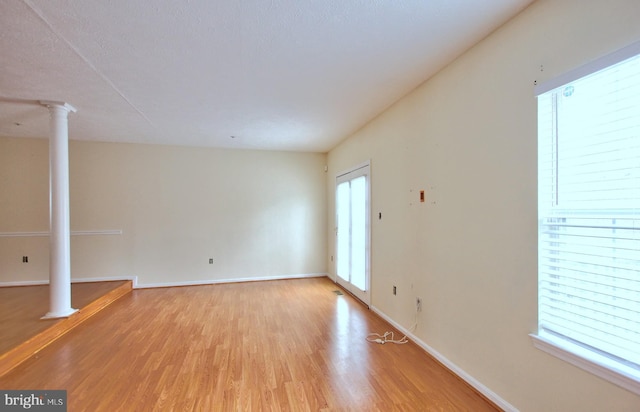 unfurnished living room featuring light wood-style floors, decorative columns, baseboards, and a wealth of natural light