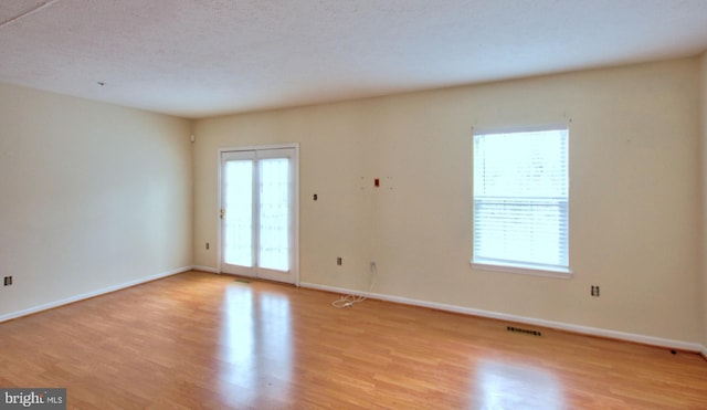 empty room featuring a textured ceiling, light wood-type flooring, visible vents, and baseboards