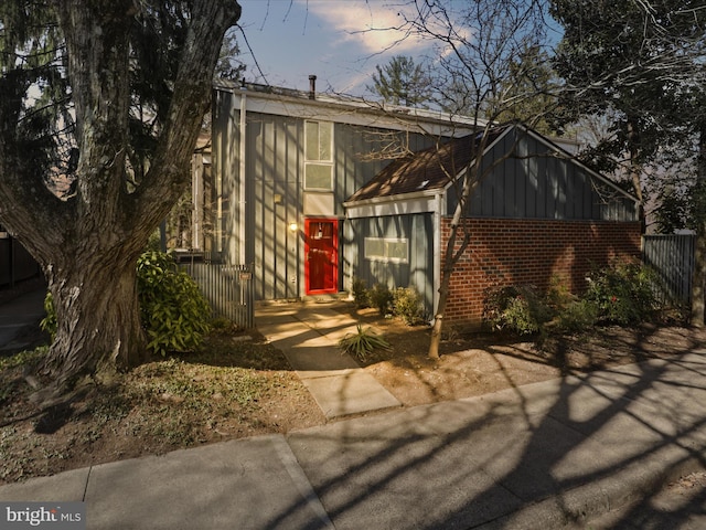 view of front of home featuring board and batten siding, brick siding, and fence