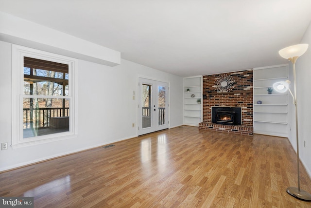 unfurnished living room with a brick fireplace, light hardwood / wood-style floors, and built in shelves