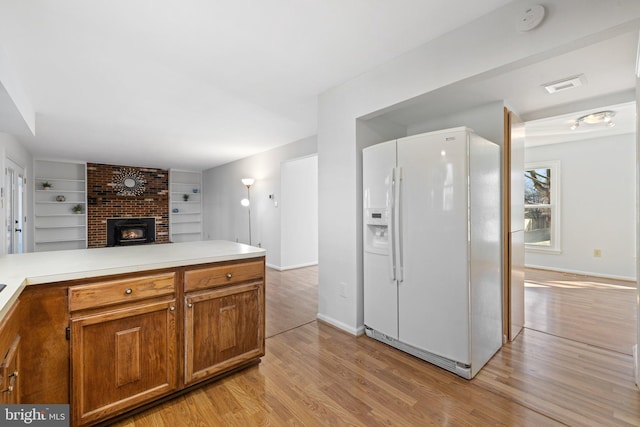 kitchen with white fridge with ice dispenser, kitchen peninsula, built in shelves, and light hardwood / wood-style flooring