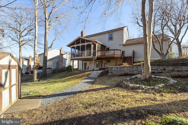 rear view of property featuring a storage unit, a sunroom, a lawn, and a wooden deck