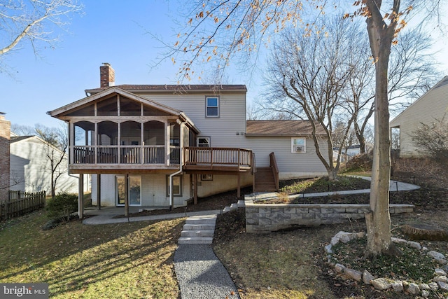 back of property featuring a lawn, a patio area, a deck, and a sunroom