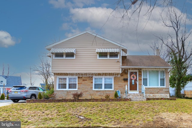 tri-level home featuring a front yard, a chimney, and a shingled roof