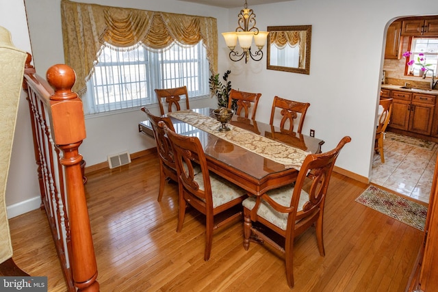 dining space with light wood-style flooring, arched walkways, visible vents, and baseboards