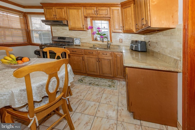 kitchen with under cabinet range hood, stainless steel gas stove, brown cabinetry, and a sink