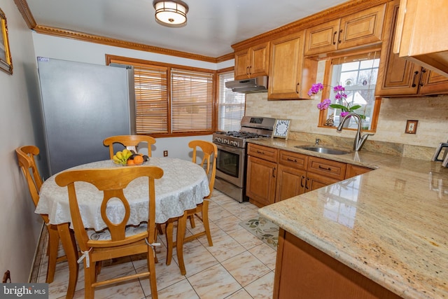 kitchen featuring brown cabinetry, a sink, under cabinet range hood, appliances with stainless steel finishes, and backsplash