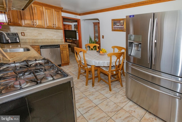 kitchen featuring tasteful backsplash, ornamental molding, appliances with stainless steel finishes, arched walkways, and brown cabinetry