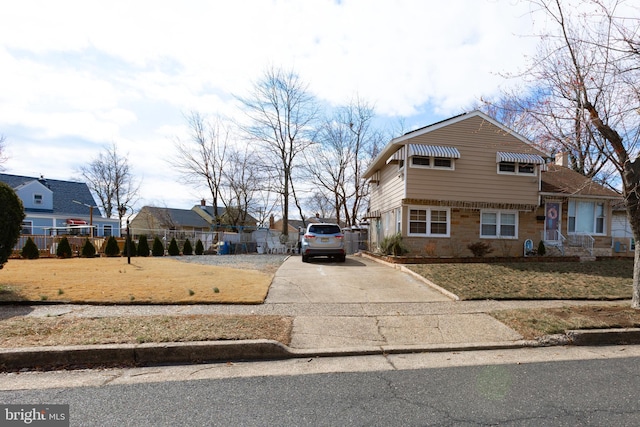 view of front of house with brick siding, driveway, and fence