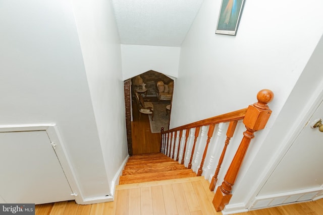 staircase featuring arched walkways, wood finished floors, baseboards, and a textured ceiling