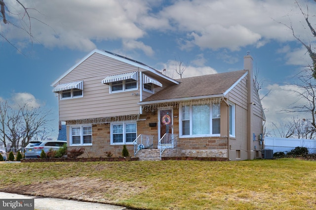 split level home featuring central air condition unit, stone siding, a front yard, a shingled roof, and a chimney