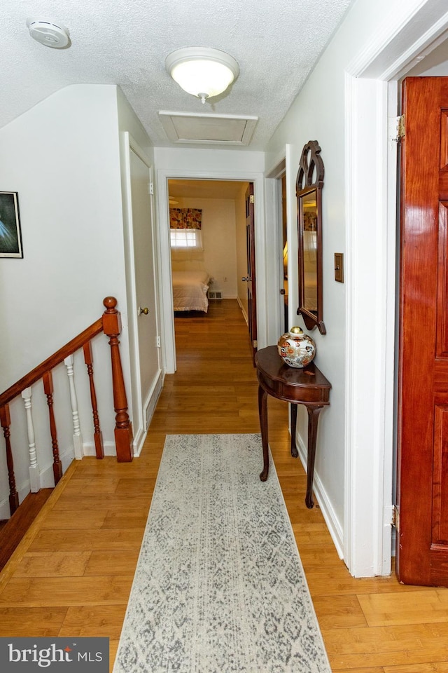 corridor with a textured ceiling, attic access, and light wood finished floors