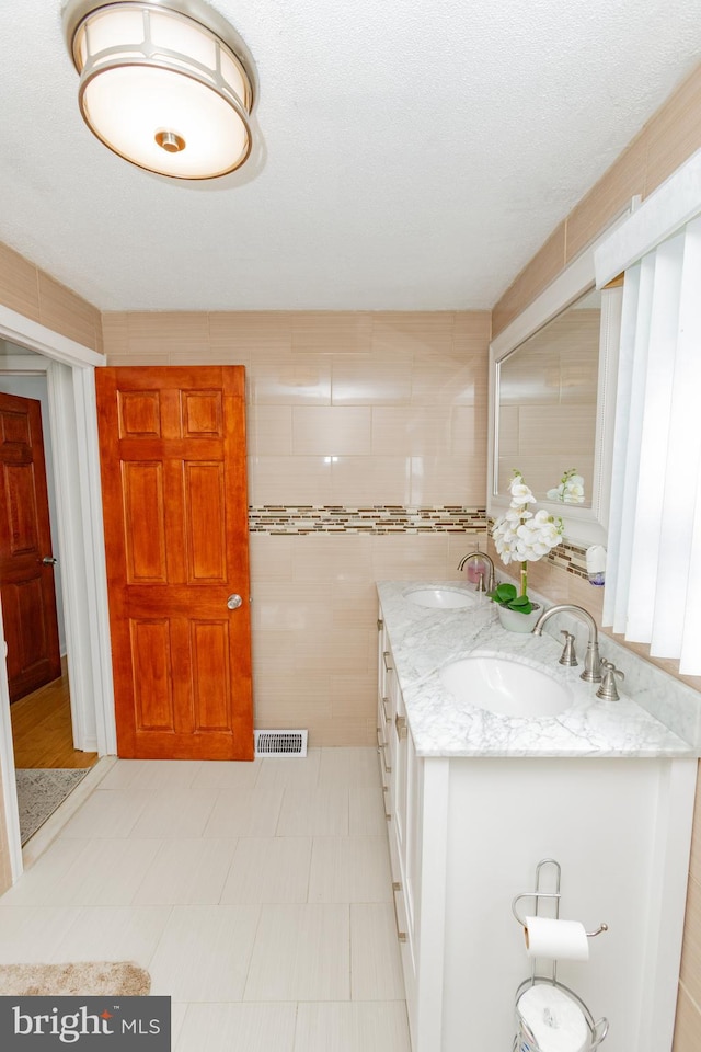 kitchen featuring a sink, visible vents, light stone countertops, and tile walls