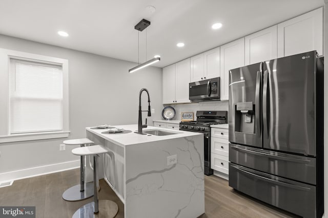 kitchen featuring a center island with sink, white cabinets, decorative light fixtures, light stone countertops, and stainless steel appliances