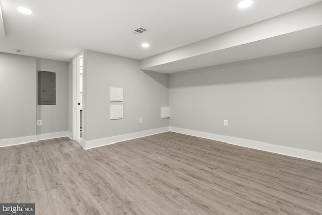 finished basement featuring light wood finished floors, baseboards, electric panel, and visible vents