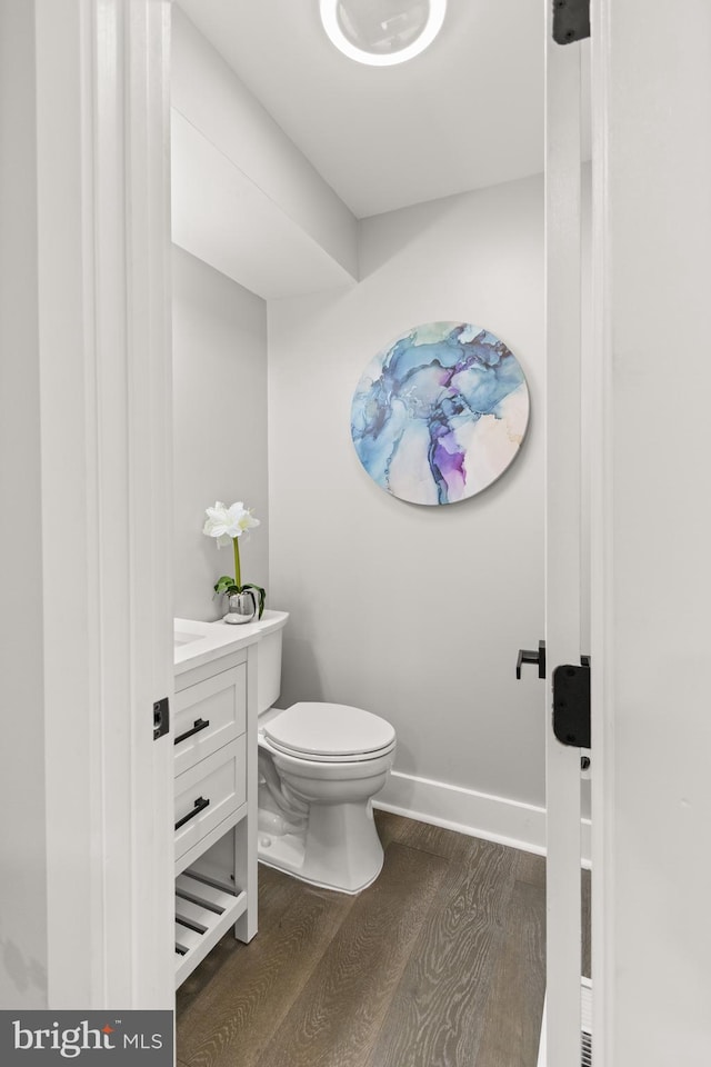 half bath with baseboards, vanity, toilet, and wood finished floors